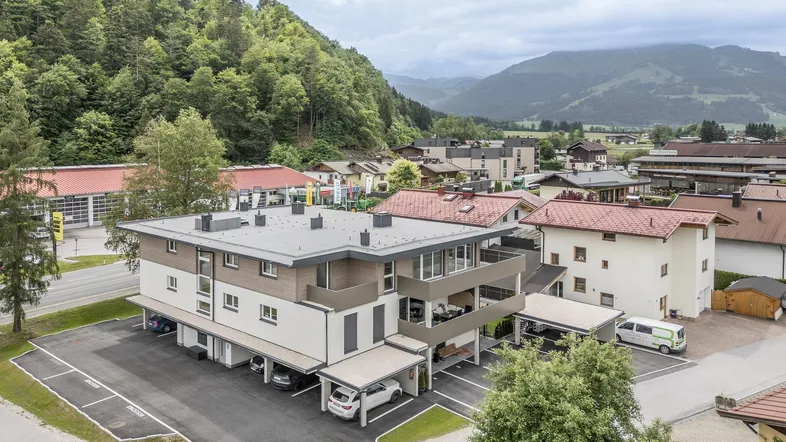 Moderne Wohnanlage in alpiner Umgebung mit Parkplätzen und Bergblick.