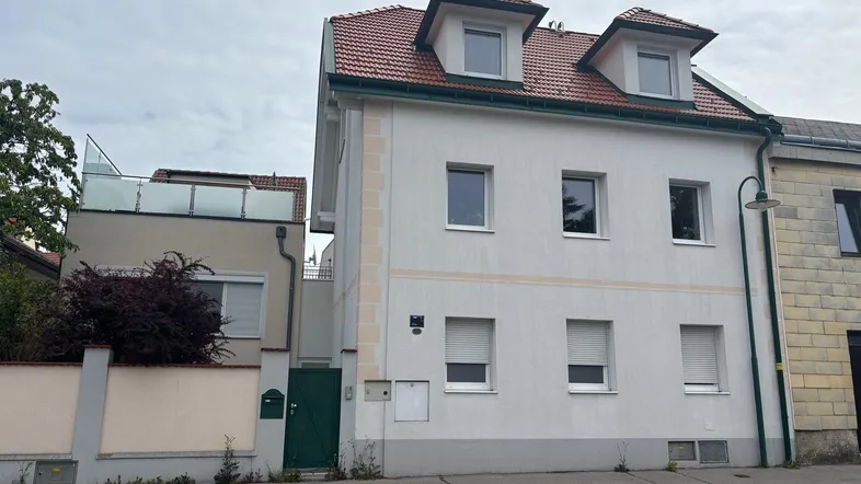 Weiß verputztes Wohnhaus mit roten Dachziegeln und Rollläden an den Fenstern.