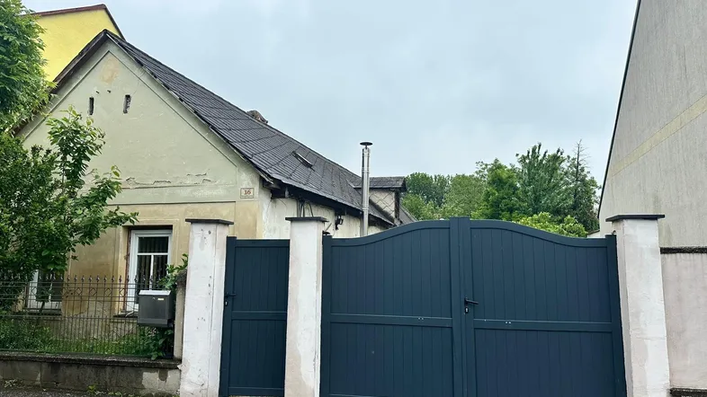 Altes Haus mit Putzschäden und einem modernen, dunklen Tor zur Straße hin.