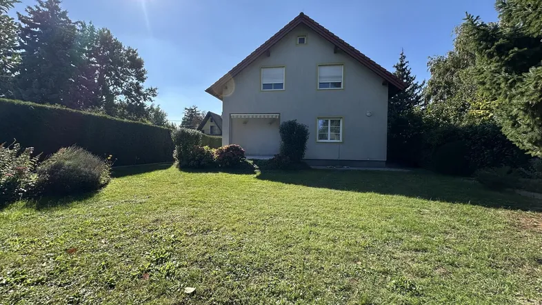 Einfamilienhaus mit großem Rasen und gepflegtem Garten unter strahlendem Sonnenschein.