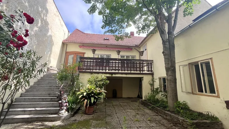 Hinterhof mit gepflastertem Bereich, Treppe zum oberen Balkon und üppiger Vegetation.