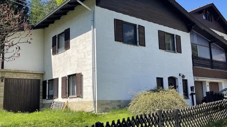 Weißes Einfamilienhaus mit braunen Fensterläden und Satteldach in ländlicher Umgebung.