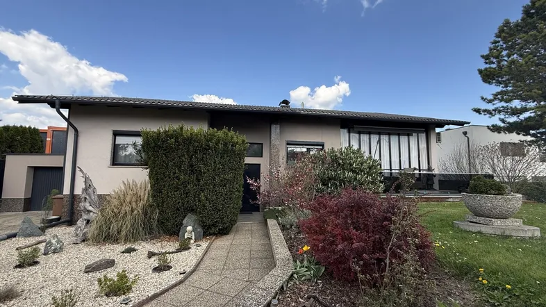 Einfamilienhaus mit gepflegtem Vorgarten, Kiesbeet und üppiger Bepflanzung unter blauem Himmel.