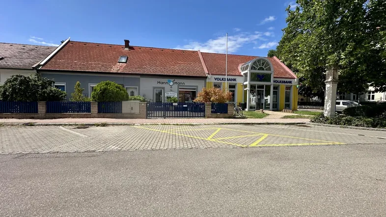 Gebäudeansicht mit Geschäftsfassaden und Parkplätzen unter blauem Himmel.