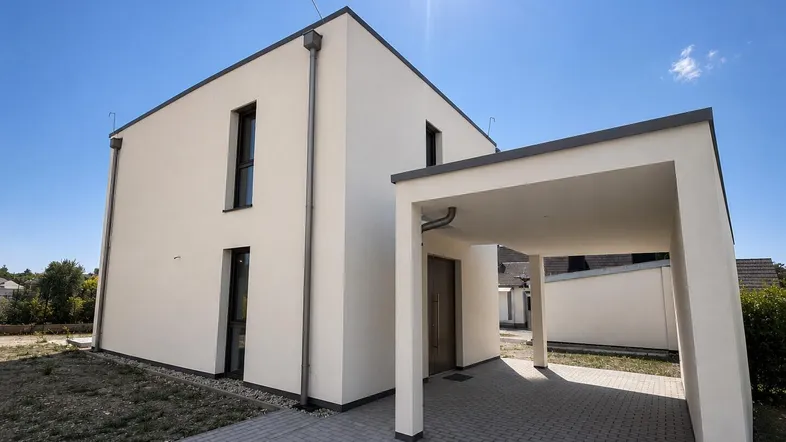 Modernes Einfamilienhaus mit heller Fassade und integriertem Carport unter blauem Himmel.
