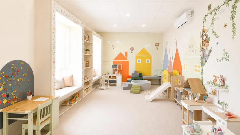 Heller und freundlicher Spielraum mit bunten Wandmalereien, Kindermöbeln und einer gemütlichen Leseecke am Fenster.