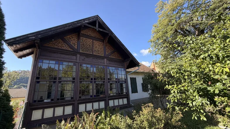 Historisches Gebäude mit einem charmanten Wintergarten und kunstvollen Holzarbeiten unter blauem Himmel.