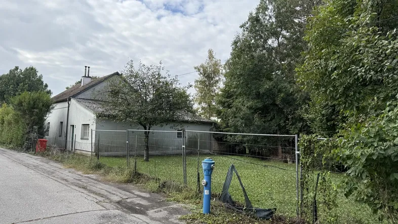 Altes Haus mit umzäuntem Grundstück und viel Grün in ländlicher Umgebung.
