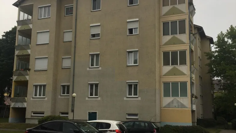 Mehrstöckiges Apartmentgebäude mit mehreren Balkonen und gepflegter Außenanlage unter bewölktem Himmel.