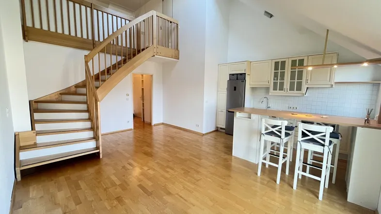 Heller offener Wohnbereich mit integrierter Küche, Holztreppe und Dachschrägen.
