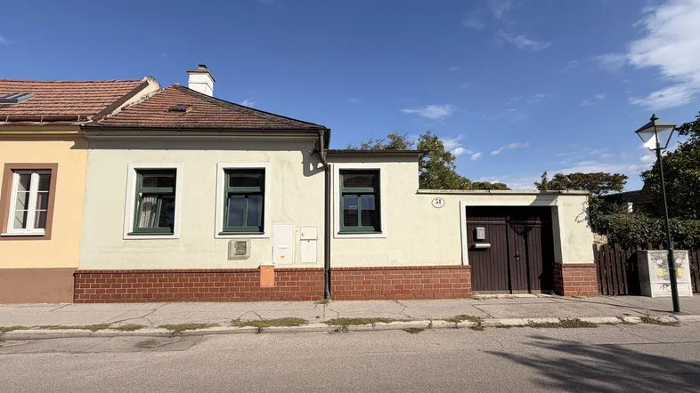 Fassade eines traditionellen Hauses mit grünen Fenstern und einem Garagentor von der Straße aus.