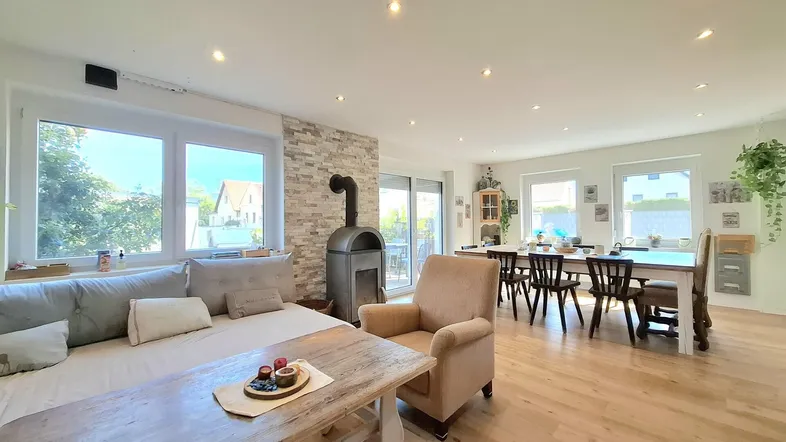 Helles Wohn- und Esszimmer mit Holzboden, Kaminofen und Zugang zur Terrasse.