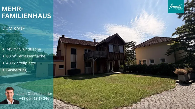 Mehrfamilienhaus mit großem Garten und gepflasterter Auffahrt unter blauem Himmel.