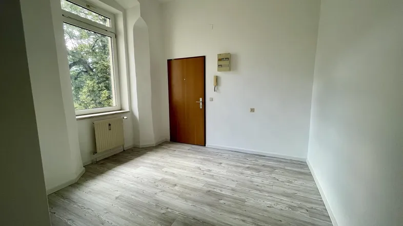 Helles Zimmer mit Laminatboden und großem Fenster, das viel Tageslicht hereinlässt.