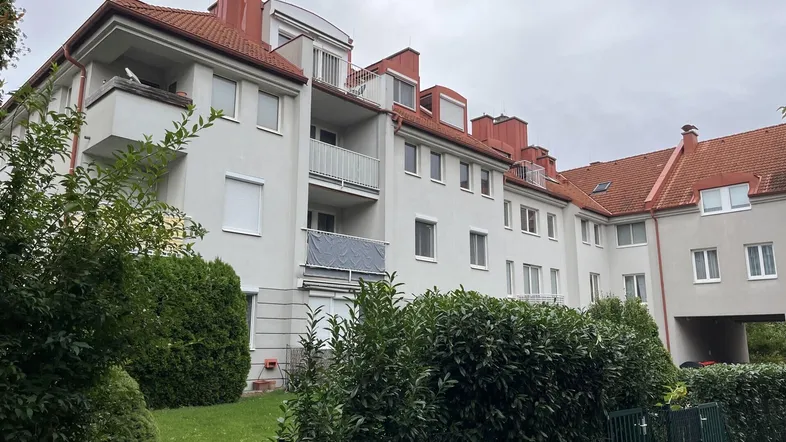Mehrfamilienhaus mit weißer Fassade, roten Ziegeldächern und gepflegter Hecke im Vordergrund.