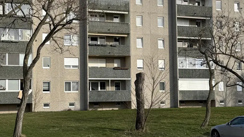 Mehrfamilienhaus mit Balkonen und Grünflächen, umgeben von Bäumen und einem Parkplatz.