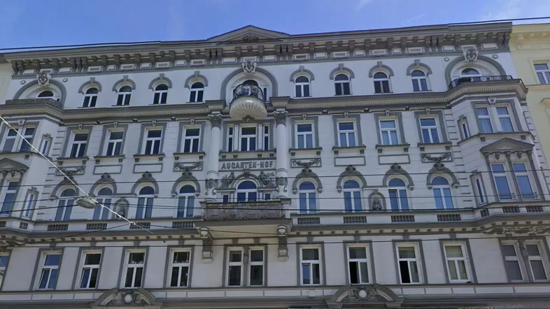 Historisches Gebäude mit reich verzierter Fassade, großen Fenstern und einem kleinen Balkon.