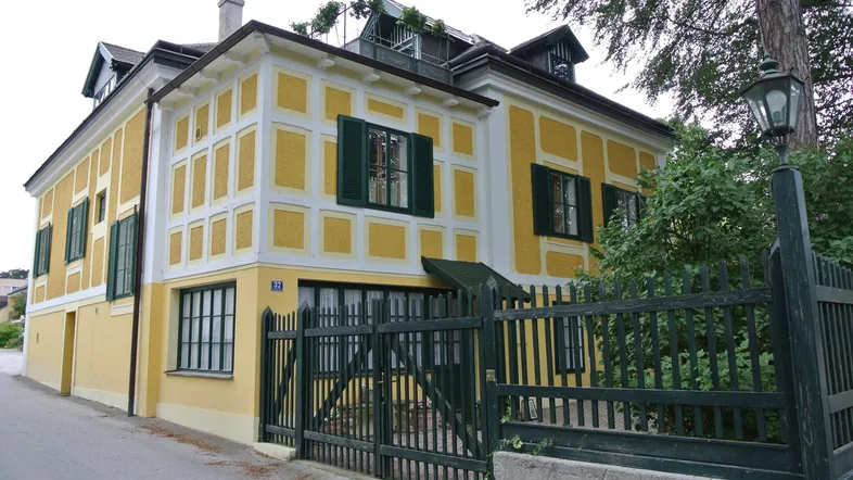 Traditionelles Gebäude mit gelber Fassade, weißen Akzenten und grünen Fensterläden.