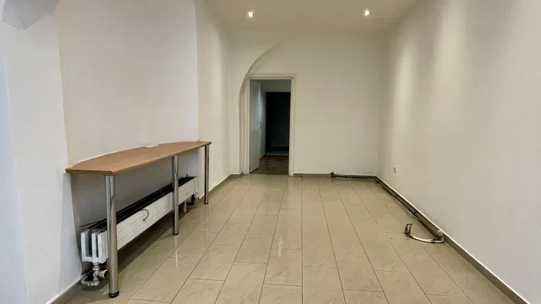 Geräumiger, leerer Raum mit hellen Fliesen, weißen Wänden und Einbaustrahlern an der Decke.