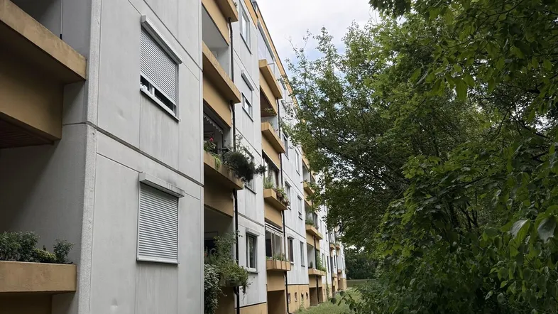 Mehrfamilienhaus mit Balkonen und grüner Umgebung, umgeben von Bäumen und Sträuchern.