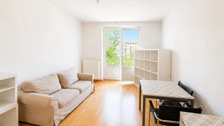Helles Wohnzimmer mit Parkettboden, Sofa, Esstisch und Zugang zum Balkon.