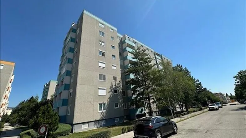 Mehrstöckiges Wohngebäude mit blauen Akzenten und umliegender Grünfläche unter blauem Himmel.