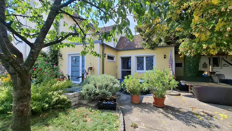 Idyllischer Gartenbereich mit Terrasse und üppiger Vegetation, umgeben von Bäumen und Sträuchern.