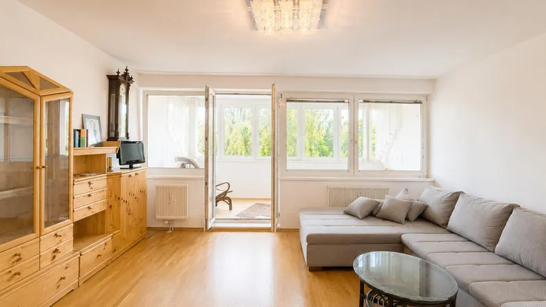 Helles Wohnzimmer mit Parkettboden, bequemer Couch und Zugang zu einem verglasten Balkon.