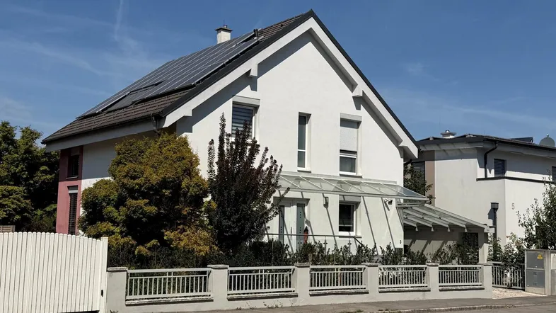 Modernes Einfamilienhaus mit weißer Fassade, Satteldach und Photovoltaikanlage auf dem Dach.