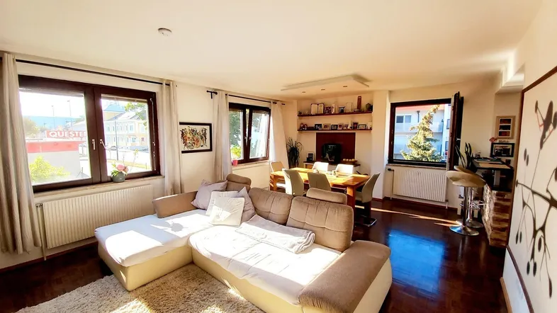 Helles Wohn- und Esszimmer mit großem Ecksofa, Esstisch und Blick nach draußen.
