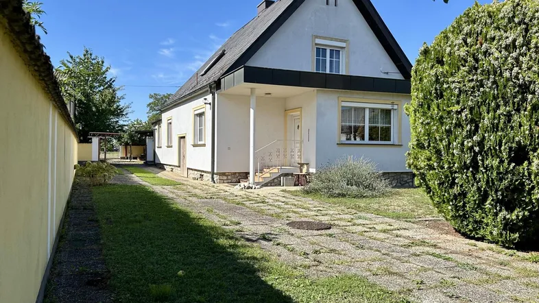 Einfamilienhaus mit Satteldach, Vorgarten und gepflasterter Einfahrt unter blauem Himmel.