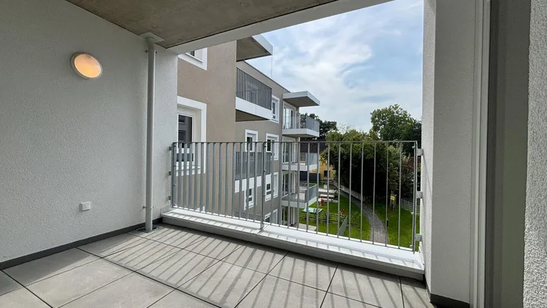 Geräumiger Balkon mit Fliesenboden und Blick auf die umliegenden Gebäude und Grünflächen.