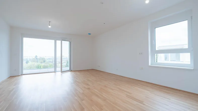 Helles Wohnzimmer mit Parkettboden, großen Fenstern und Zugang zu einem Außenbereich.