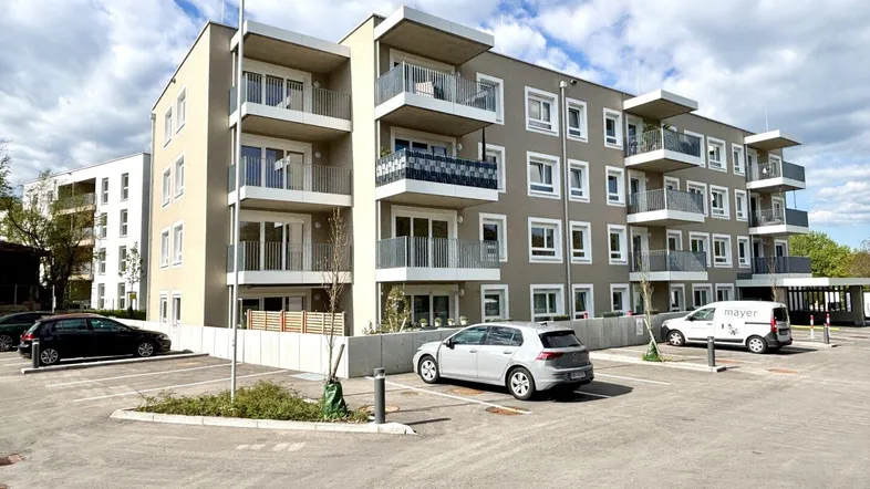 Modernes Mehrfamilienhaus mit mehreren Balkonen und Außenparkplätzen unter bewölktem Himmel.