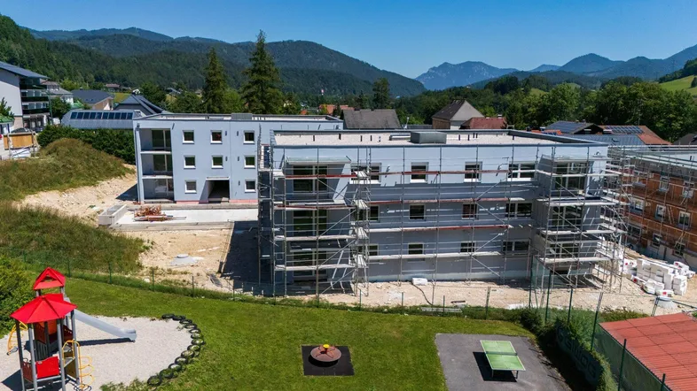 Neubauwohnungen im Bau mit Kinderspielplatz und Bergblick in ländlicher Umgebung.