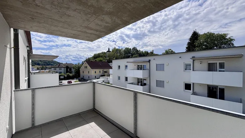Geräumiger Balkon mit Fliesenboden und Blick auf die umliegende Wohngegend und einen Hügel.
