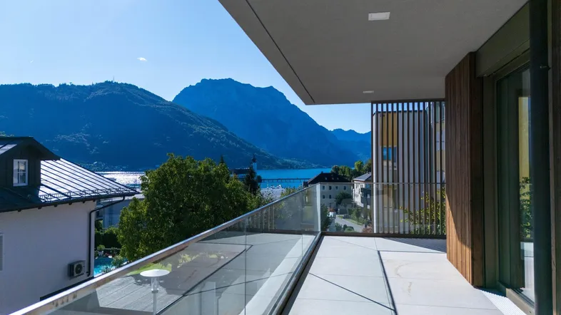 Geräumiger Balkon mit Glasgeländer und atemberaubendem Blick auf den See und die umliegenden Berge.
