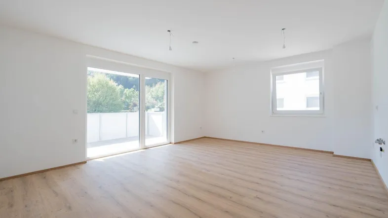Helles Zimmer mit Laminatboden, weißen Wänden und Zugang zu einem Balkon oder einer Terrasse.