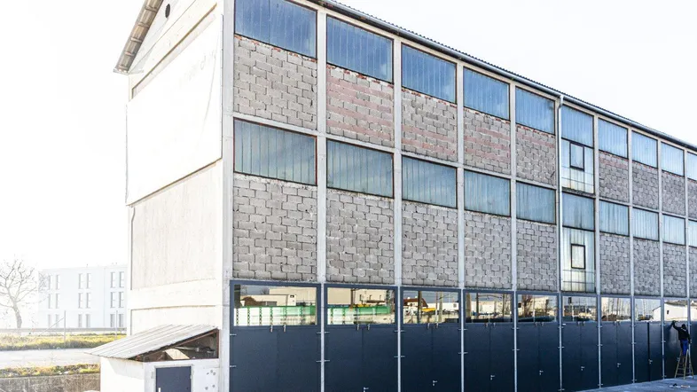 Industrielles Gebäude mit Betonfassade, großen Glasfenstern und mehreren dunklen Lagertoren im Erdgeschoss.