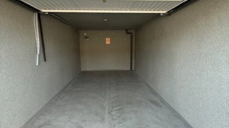 Leere Einzelgarage mit Betonboden und weißem Sektionaltor, bereit zur Nutzung.