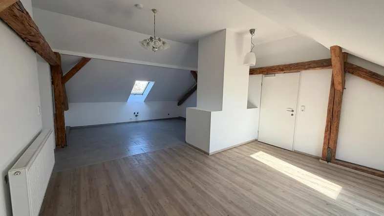 Helles Dachgeschosszimmer mit sichtbaren Holzbalken, Laminatboden und Dachfenster.