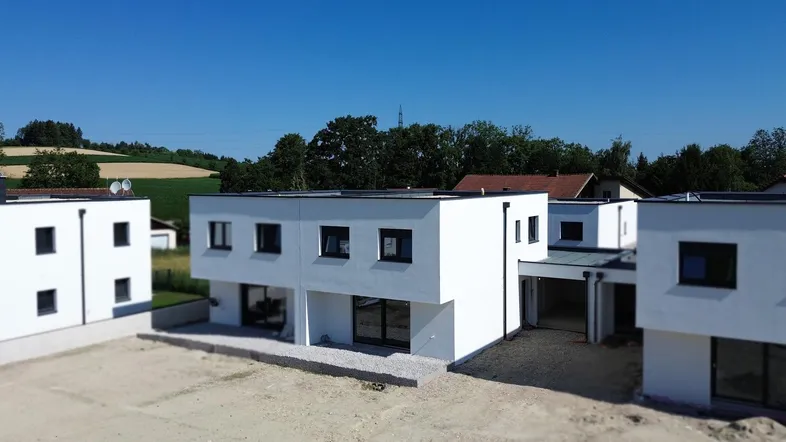 Moderne Neubauten mit Flachdächern in ländlicher Umgebung unter blauem Himmel.