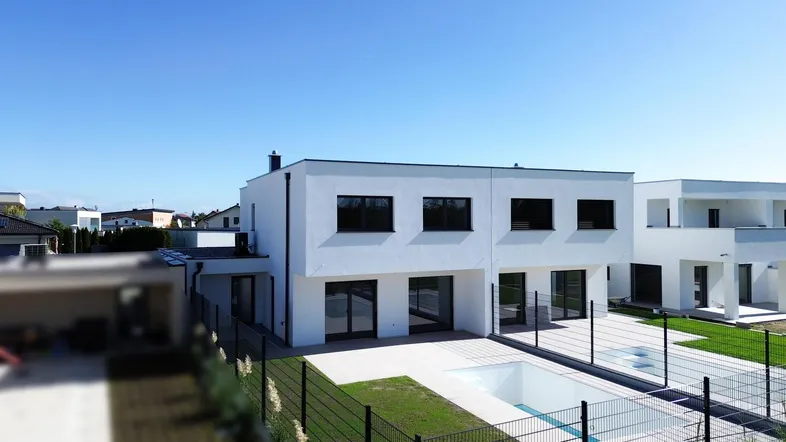Moderne weiße Villa mit Flachdach, Garten und integriertem Pool in sonniger Lage.