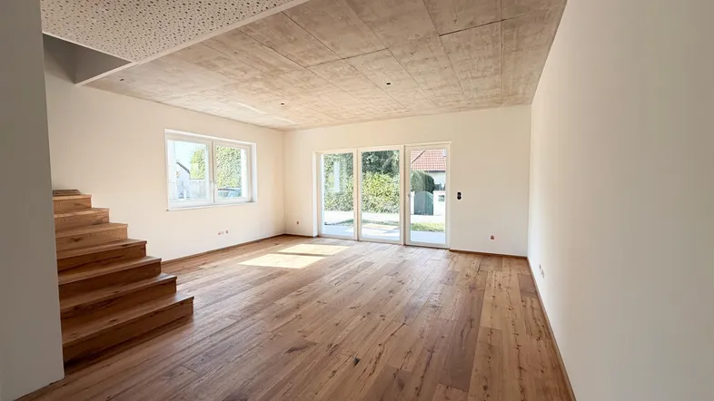 Helles Wohnzimmer mit Holzboden, Betondecke und Zugang zum Garten.
