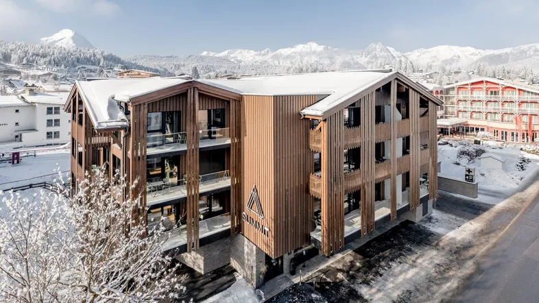 Modernes Gebäude mit Holzfassade und Balkonen, eingebettet in eine verschneite Berglandschaft.