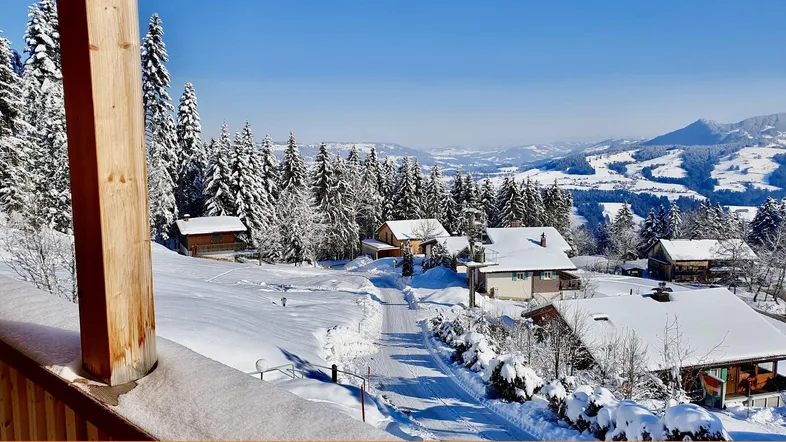 Winterliche Berglandschaft mit verschneiten Häusern und weitem Blick über die Täler.