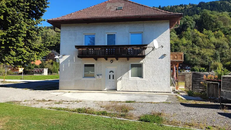 Vorderansicht des Hauses mit Balkon und Blick auf die umliegende Natur unter blauem Himmel.