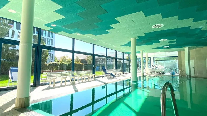 Großzügiger Innenpoolbereich mit großen Fenstern, die viel Tageslicht hereinlassen und einen Blick ins Grüne bieten.