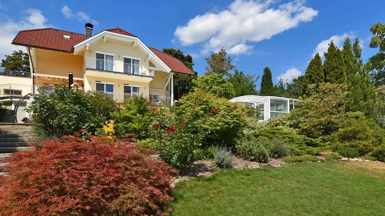 Großzügiges Anwesen mit gepflegtem Garten, Poolüberdachung und sonniger Fassade unter blauem Himmel.