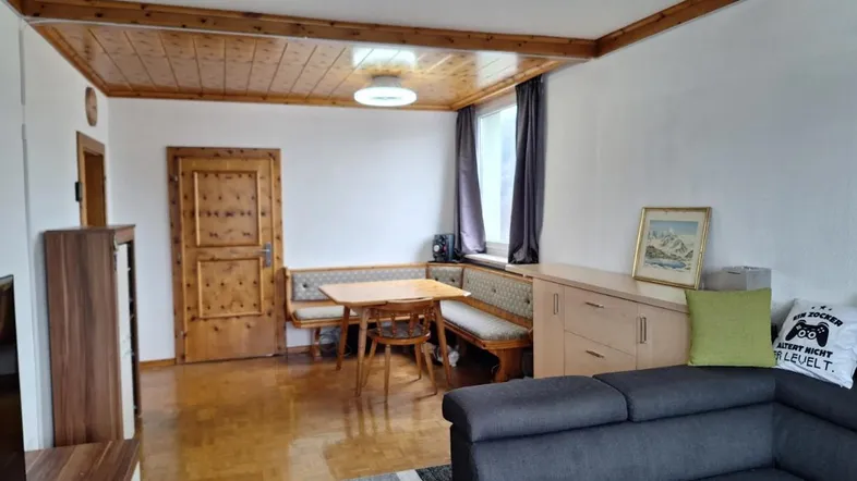 Gemütlicher Wohn-Essbereich mit Holzbalkendecke, Parkettboden und traditioneller Sitzecke am Fenster.